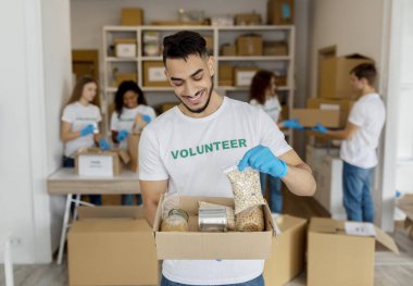 Milenyum erkek gönüllü hayır kurumunda çalışıyor, bağış kutusunu tutuyor, hayır kurumunda çalışmaktan gurur duyuyor.