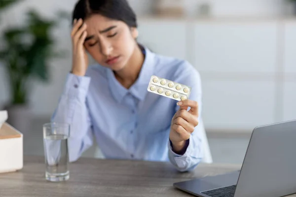 Señorita india triste desesperada que sufre de dolor, migraña y enfermedad en el lugar de trabajo con el ordenador portátil sostiene pastillas — Foto de Stock