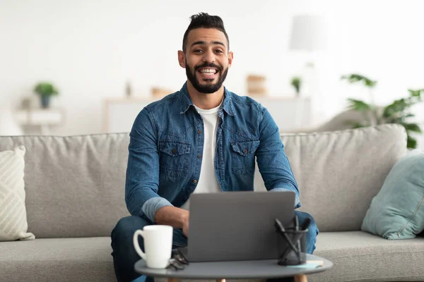 Araber sitzt mit Laptop auf Couch, nimmt an Webvorlesung oder Videokonferenz teil, arbeitet oder studiert online — Stockfoto