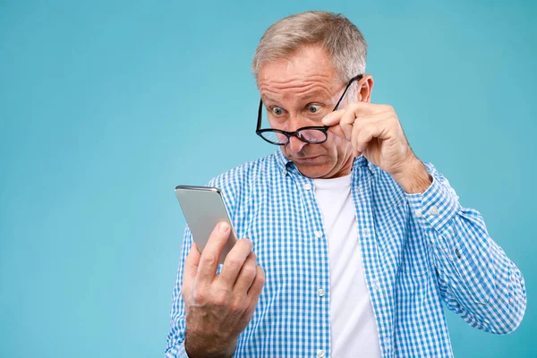 Sorprendido hombre maduro utilizando el teléfono móvil, mirando a la pantalla —  Fotos de Stock