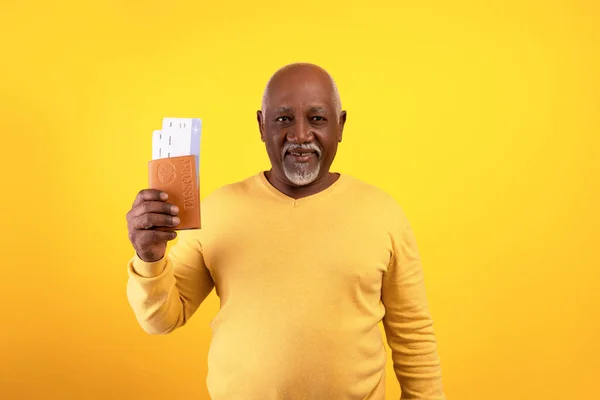 Koncepcja tanich lotów. Szczęśliwy starszy czarny człowiek posiadający paszport i bilety, stojący na pomarańczowym tle studio — Zdjęcie stockowe