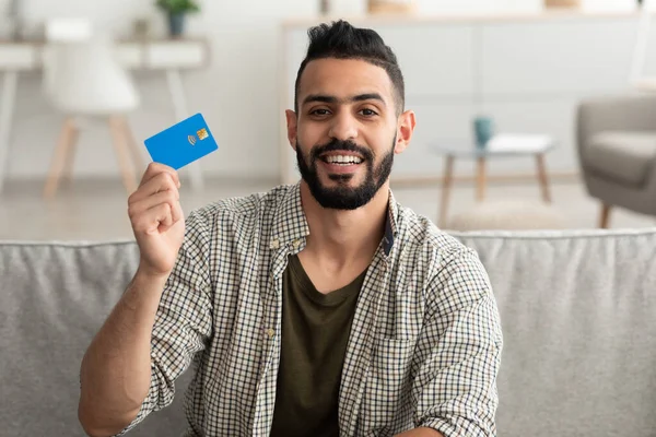 Snadné bezkontaktní platby. Portrét radostného mladého Araba s kreditní kartou při pohledu do kamery uvnitř — Stock fotografie