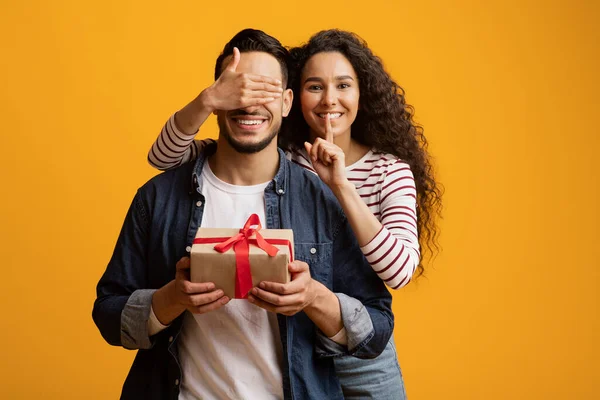 Liebevolle junge Frau bedeckt Boyfriends Augen und überrascht ihn mit Geschenk — Stockfoto
