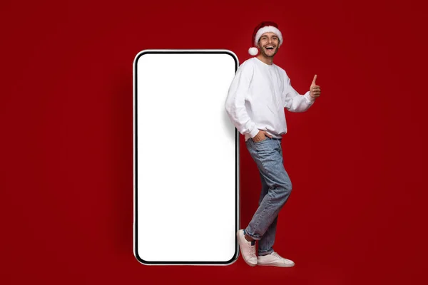 Świetna oferta. Podekscytowany człowiek w Santa kapelusz stojący blisko Big Blank Smartphone — Zdjęcie stockowe