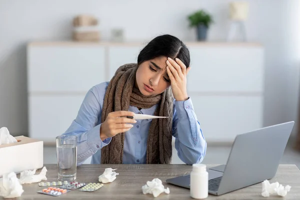 Sad young hindu woman manager suffering from headache, colds and flu looks at thermometer — Stock Photo, Image