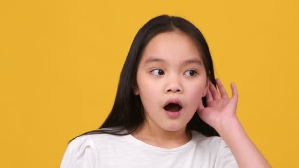 Unger er nysgjerrige. Closeup portrett av opphisset liten jente som overhører taster, lytter med hånden nær ører på begge sider – stockvideo