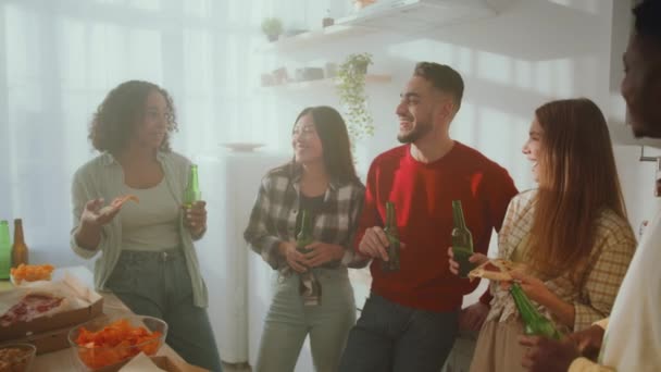 Группа веселых молодых многонациональных друзей, наслаждающихся вместе выходными, поедающих пиццу с пивом и смеющихся над кухней — стоковое видео