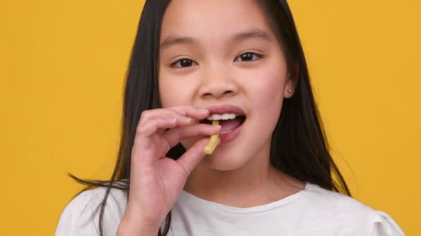 Діти їдять звички. Чарівна маленька азіатська дівчинка їсть смачну картоплю фрі, насолоджуючись фаст-фудом, дивлячись на камеру — стокове відео