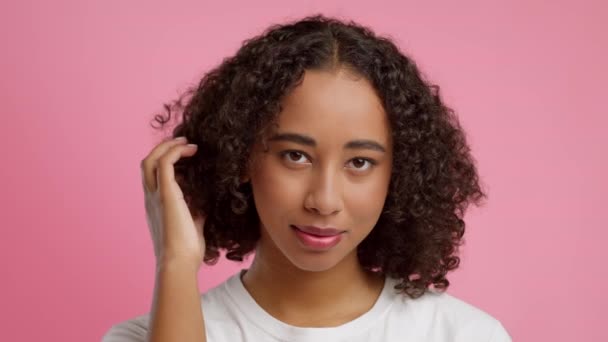 Afro-americana mujer torciendo rizo en dedo sobre rosa fondo — Vídeos de Stock