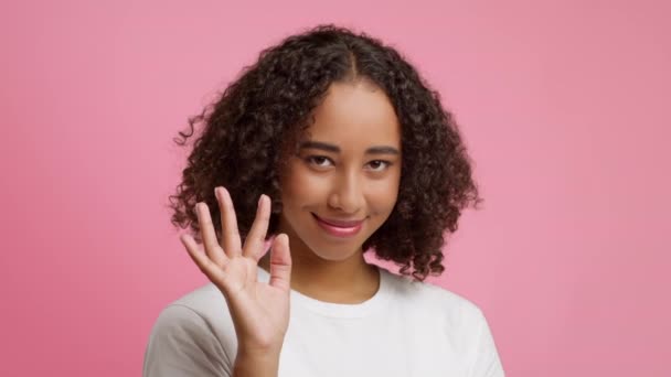 Juguetona mujer afroamericana ondeando Hello sonriendo sobre fondo rosa — Vídeos de Stock