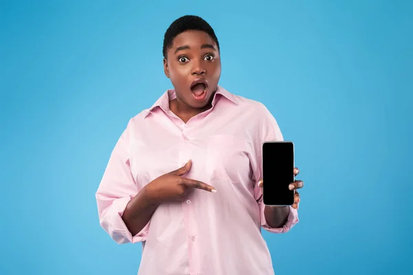 Megdöbbent afro-amerikai hölgy mutatja Smartphone üres képernyő, kék háttér — Stock Fotó