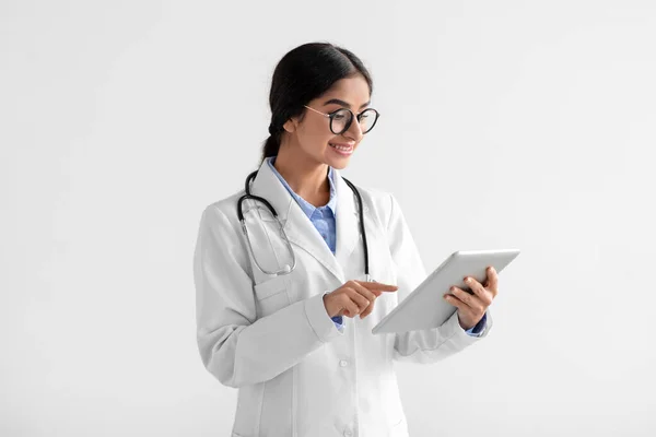 Jovem médica indiana feliz com casaco branco e óculos trabalhando em tablet — Fotografia de Stock