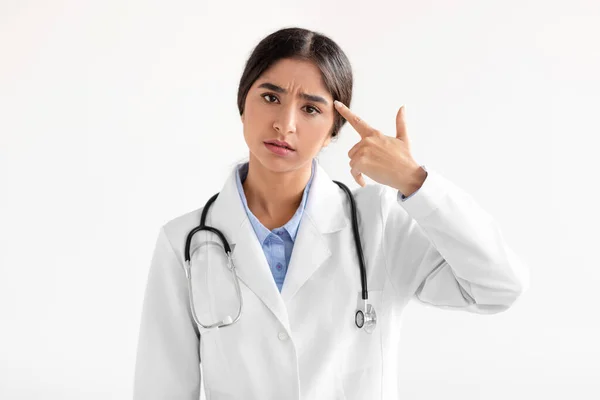 Cansado triste milenial mujer india médico en abrigo mostrar gesto de la mano, pistola cerca del templo —  Fotos de Stock