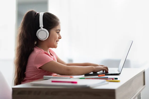 Educação online. Pequena menina do Oriente Médio em fones de ouvido usando laptop em casa — Fotografia de Stock
