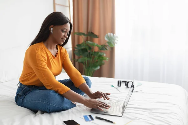 Freelancer Lady negro usando portátil usando auriculares trabajando en el dormitorio —  Fotos de Stock
