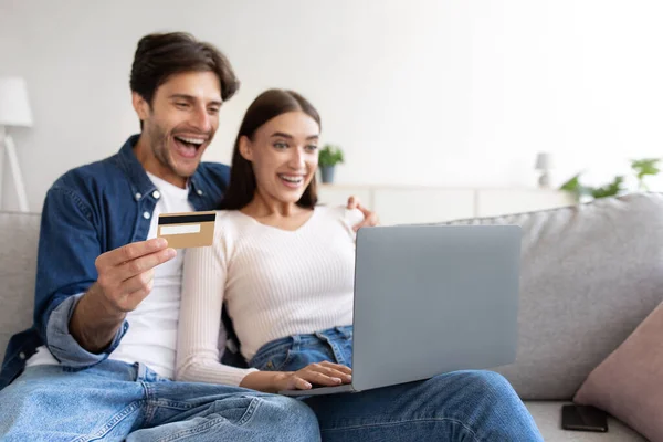 Γέλιο νεαρό ζευγάρι της Ευρώπης στον καναπέ με πιστωτική κάρτα, φορητό υπολογιστή και online ψώνια στο σαλόνι — Φωτογραφία Αρχείου