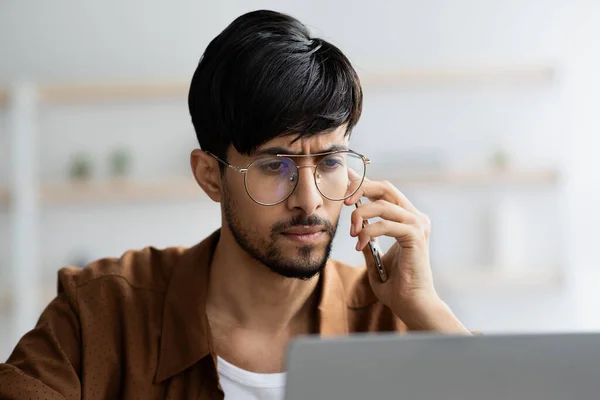 Concentrated indian manager working on laptop, having phone conversation — Stock Photo, Image