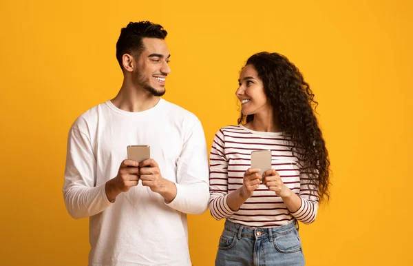Neşeli Arap adam ve kadın ellerinde akıllı telefonlar ve birbirlerine bakıyorlar. — Stok fotoğraf