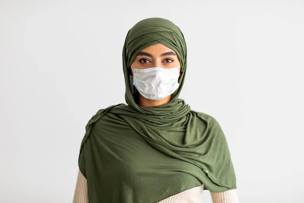 Duizendjarige Arabische vrouw in hijab met medisch masker tijdens coronavirus epidemie op lichte studio achtergrond — Stockfoto