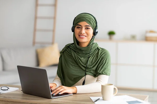 Genç tesettürlü Arap kadın bilgisayarla evden çalışıyor, kulaklık takıyor, bilgisayar kullanıyor. — Stok fotoğraf