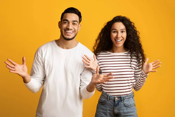 Retrato de alegre pareja árabe esparciendo las manos con emoción sobre fondo amarillo — Foto de Stock