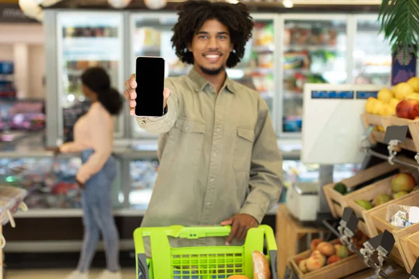 Czarny facet Wyświetlanie Smartphone pusty ekran Zakupy w supermarkecie — Zdjęcie stockowe