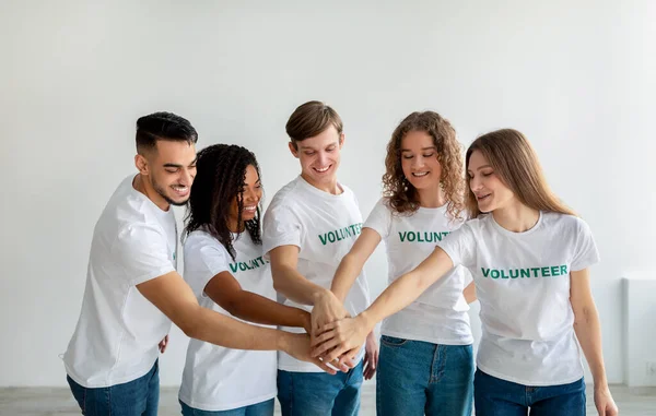 Смешанная раса молодых волонтеров, объединяющих руки вместе и улыбающихся, готовых к работе в благотворительном центре — стоковое фото