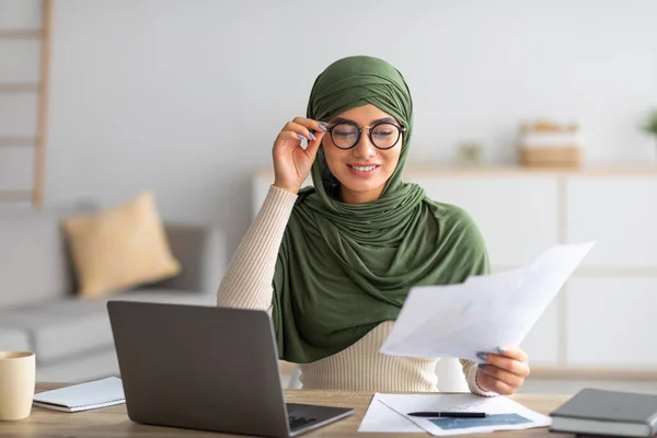 Fiatal arab női szabadúszó hidzsáb dolgozik papírok és laptop otthon — Stock Fotó