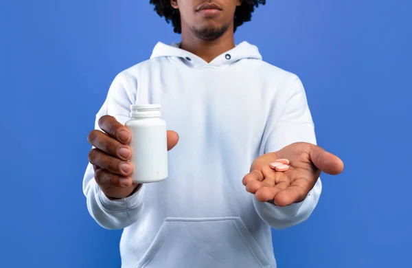 Unrecognizable black teen holding jar with meds and pills in hands on blue background. Coronavirus, cold, flu treatment — Stock Photo, Image