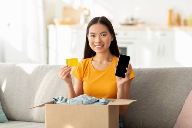 Mutlu Koreli kadın paketleri açıyor, kredi kartı ve akıllı telefonu elinde tutuyor, boş ekranlı, maket için yer gösteriyor
