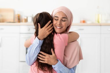 Ebeveyn sevgisi. Küçük kızını kucaklayan tesettürlü mutlu Müslüman kadın, yakın plan.