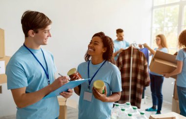 Genç erkek yönetici bağış listesini kontrol ediyor ve panoya yazı yazıyor. Mutlu gönüllülerle konuşuyor, birlikte çalışıyor.