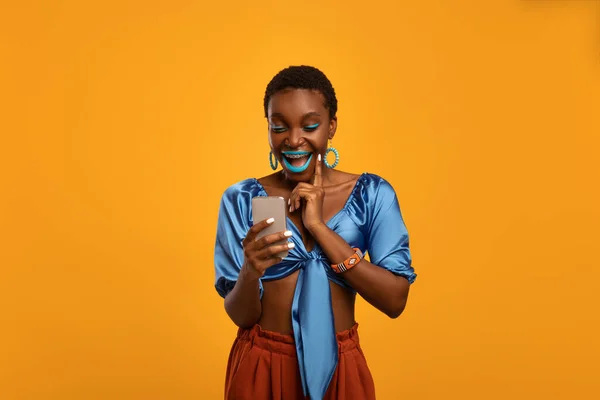 Mulher negra emocional em roupa brilhante usando smartphone — Fotografia de Stock