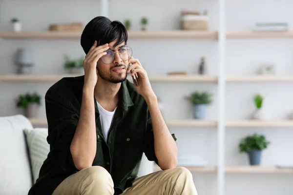 Upset indian guy having phone conversation, home interior — Stock Photo, Image