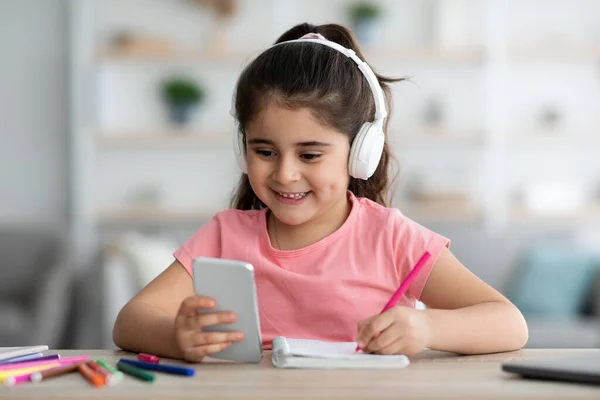 Educação Remota. Menina em fones de ouvido usando Smartphone em casa para aprendizagem à distância — Fotografia de Stock