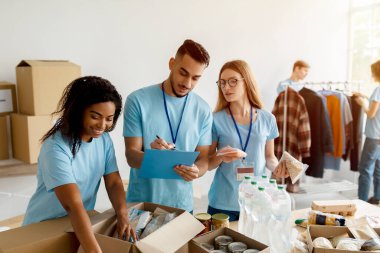 Gönüllü iş. Genç Arap erkek eylemci bağış listesini kontrol ediyor ve panoya yazıyor, gönüllüler kutuları paketliyor.