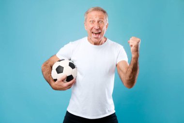 Olgun adam mavi arka planda futbol topuyla poz veriyor