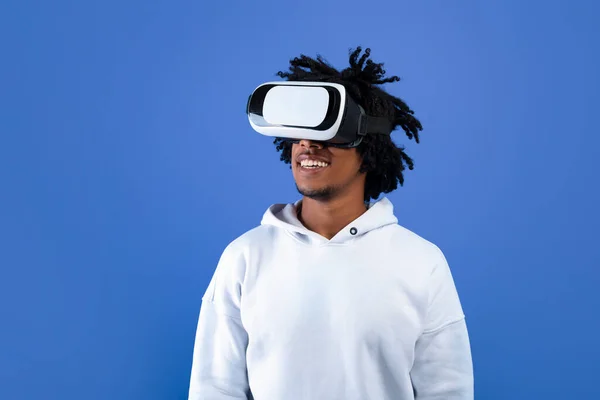 Cool Afro-Amerikaanse tiener kerel dragen VR headset, met behulp van virtual reality voor entertainment op blauwe studio achtergrond — Stockfoto