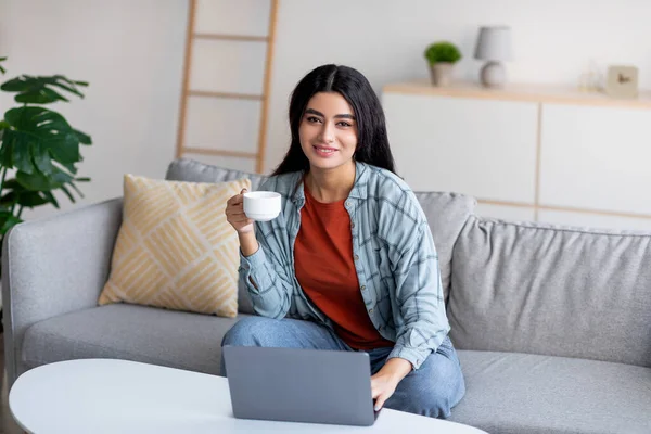 Любимая молодая арабская женщина, использующая ноутбук, учащаяся или работающая в Интернете, проводящая удаленные деловые встречи, пьющая кофе дома — стоковое фото