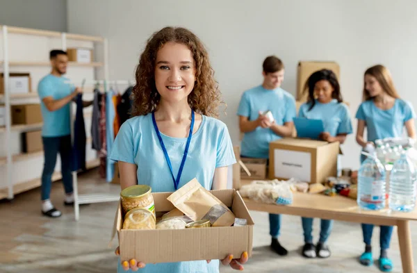 Koncept humanitární pomoci. Šťastný ženský dobrovolník v modré uniformě drží lepenkovou krabici s jídlem darování — Stock fotografie