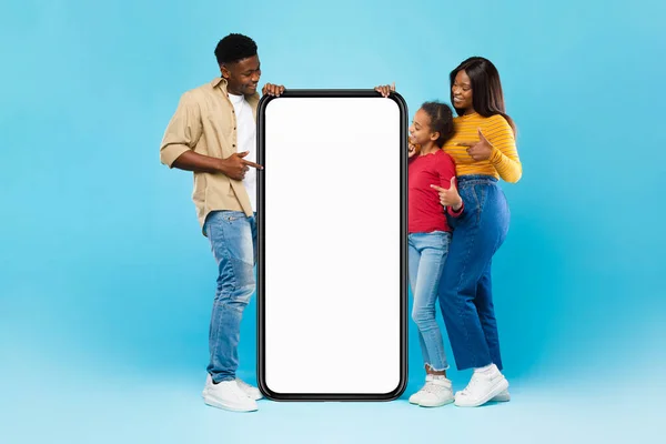 Família negra apontando para a tela grande do smartphone branco vazio, mock-up — Fotografia de Stock