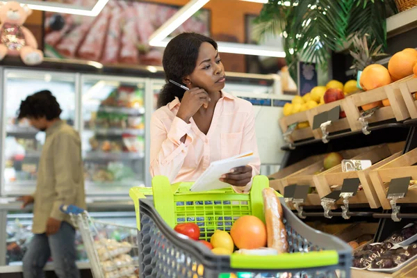 Lady Black Segurando Grocery Shopping List Calculando os preços no supermercado — Fotografia de Stock