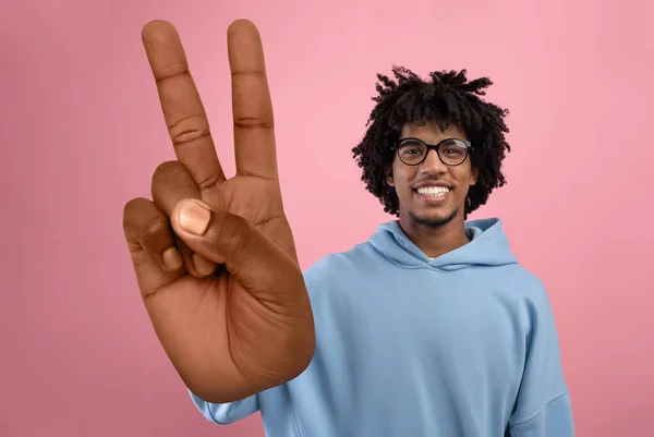 Cool African American teen guy showing big peace or victory gesture over pink studio background — Stock Photo, Image