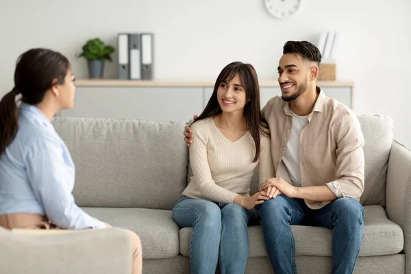 Effektiv äktenskapsterapi. Glad mellanösternpar sitter på soffan på rådgivare kontor, håller händer och ler — Stockfoto