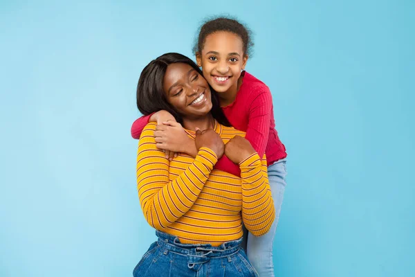 African American girl hugging her smiling mom from the back