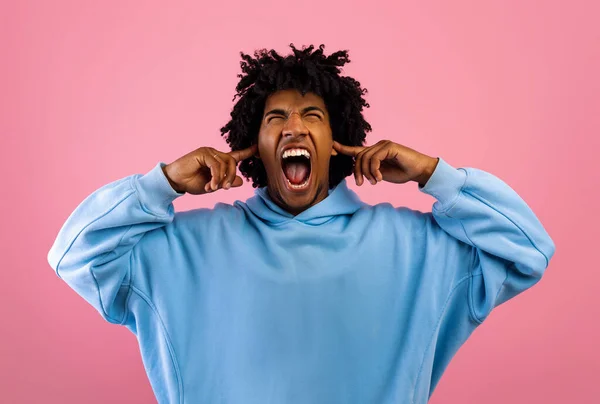 Šílený černošky teenager křičí, zakrývá uši a zavírá oči přes růžové studio pozadí — Stock fotografie