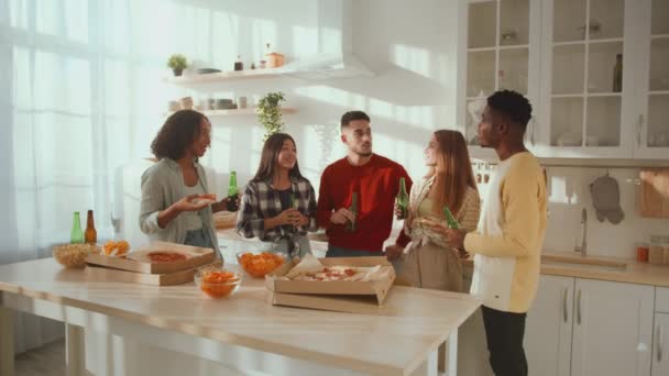 Grupa pozytywnych różnorodnych przyjaciół korzystających z wolnego czasu, rozmowy i śmiech w kuchni z piwem i pizzą, śledzenie strzał — Wideo stockowe