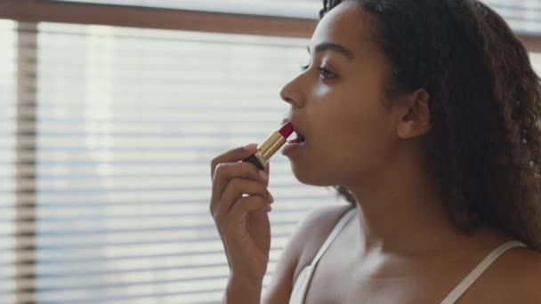 Concetto di trucco quotidiano. Vista laterale ritratto di giovane bella donna africana americana che applica rossetto rosso sulle labbra — Video Stock
