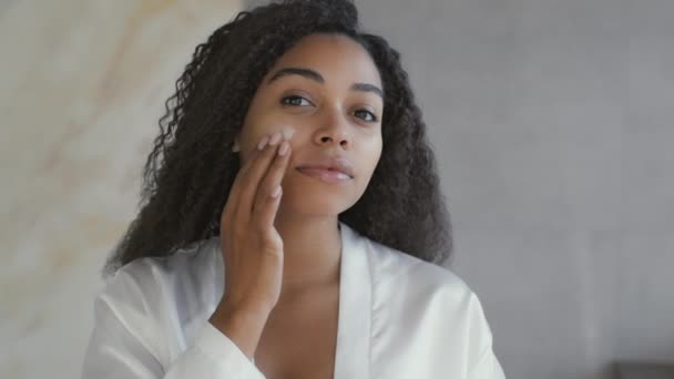 Spiegelbild einer jungen attraktiven afrikanisch-amerikanischen Dame, die feuchtigkeitsspendende Creme auf das Gesicht aufträgt und sich um das Aussehen kümmert — Stockvideo