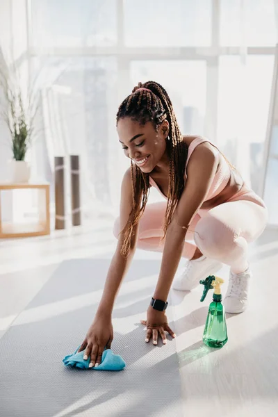 Milenial negro mujer limpieza yoga mat antes de entrenar en gimnasio —  Fotos de Stock